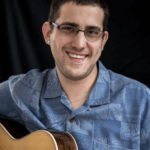 Young man with glasses holding a guitar