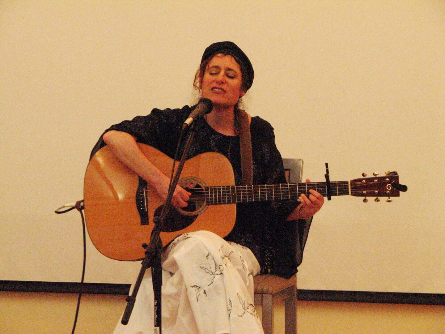 Woman playing guitar and singing at an evening session