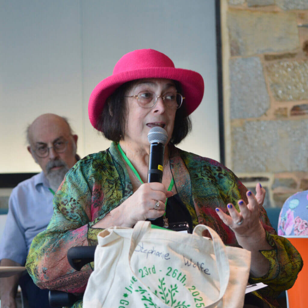 Woman in a pink hat speaking into a microphone at NewCAJE